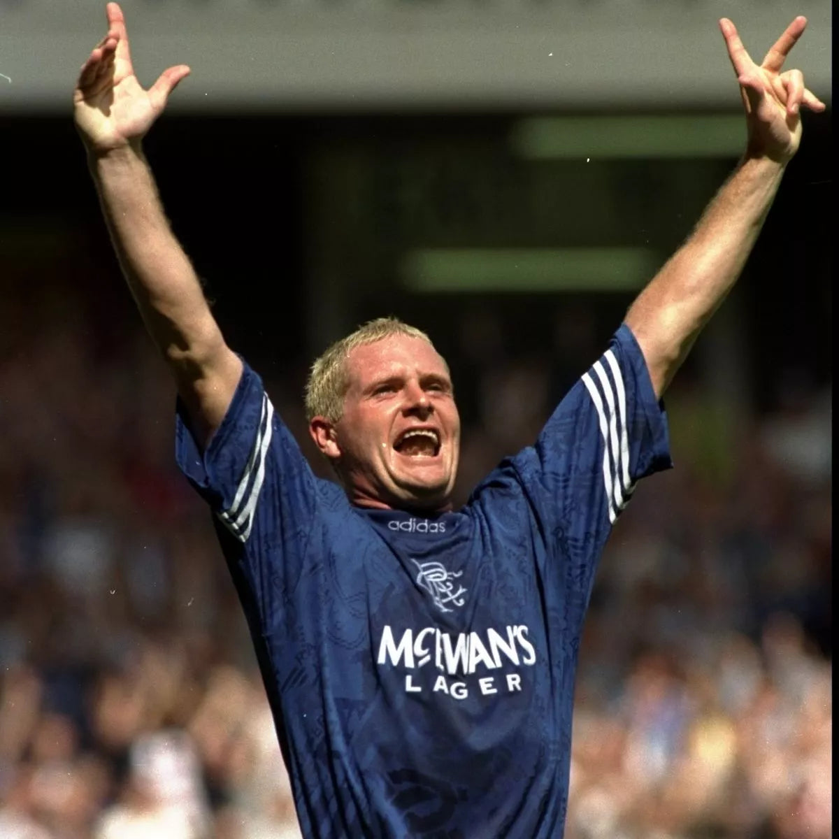 Paul Gascoigne celebrating in front of a crowd with his arms raised in a blue rangers jersey made by adidas and sponsored by McEwan's lager