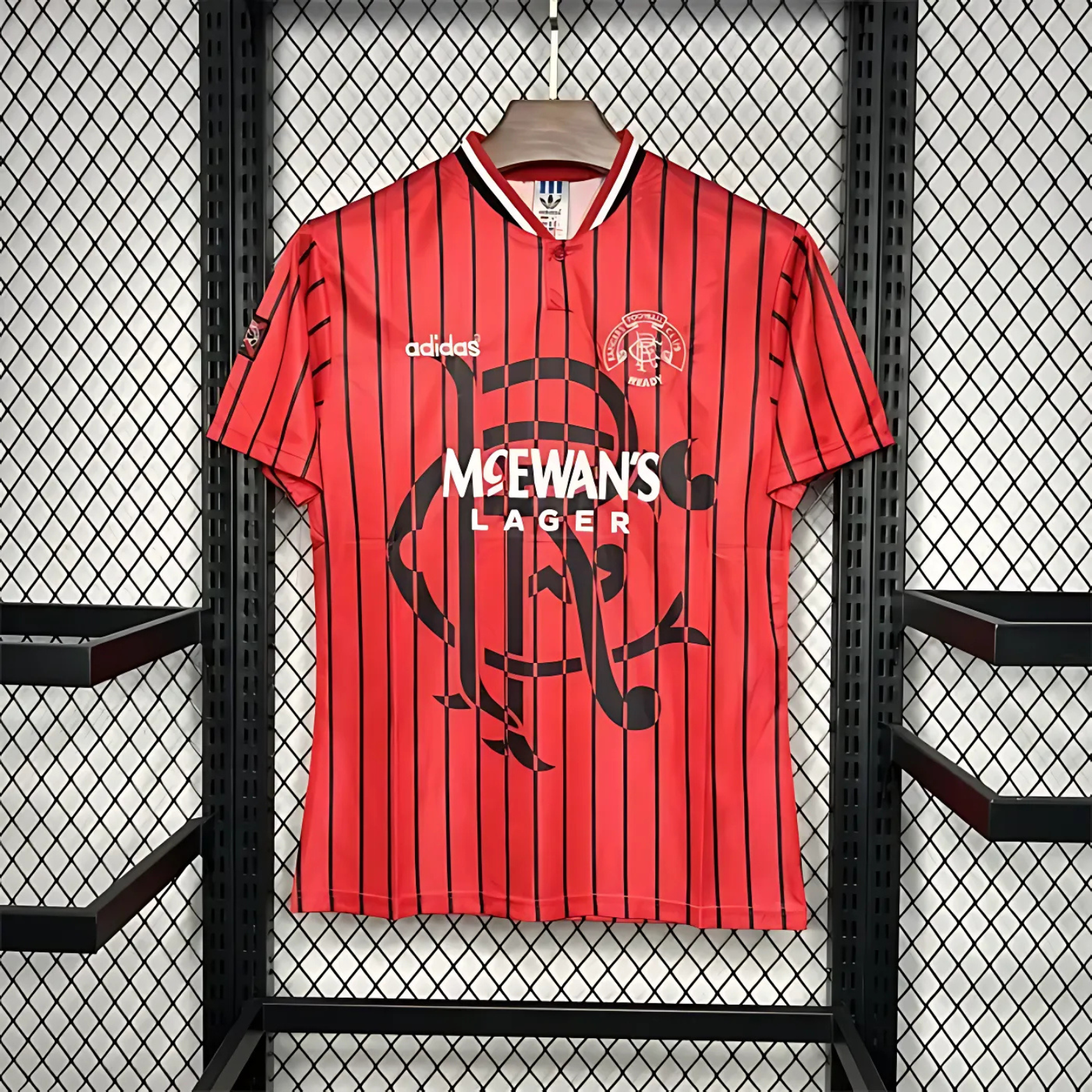 Red Rangers FC football away jersey from 1994/95 with black stripes, made by Adidas and sponsored by McEwan's lager on a hanger against a grid background