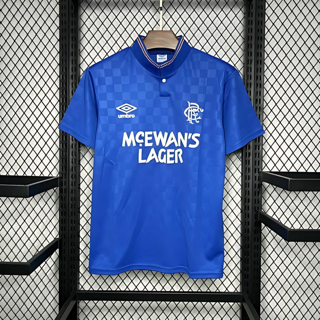 Blue Rangers Home sports jersey from 1987/90 with 'McEwan's Lager' text and Umbro logo on a hanger against a grid background