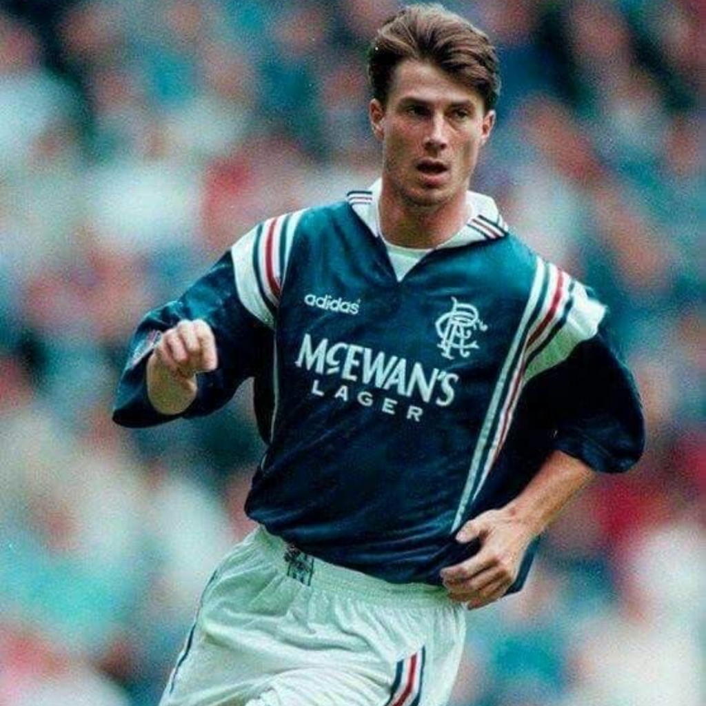 Blue Rangers football jersey with white and red stripes from 1996/97 made by adidas sponsored by McEwan's lager being worn by Brian Laudrup during a football match in front of fans